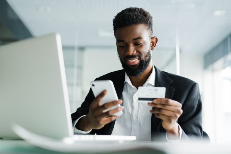 African American man paying with credit card online while making orders via mobile Internet making transaction using mobile bank application